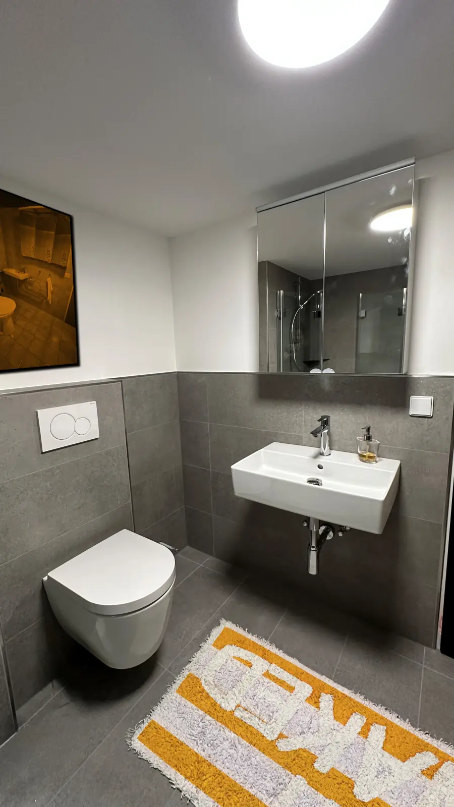 Nachher: umgestaltetes Badezimmer mit grauen Großformatfliesen, wandhängendem WC und Waschtisch.