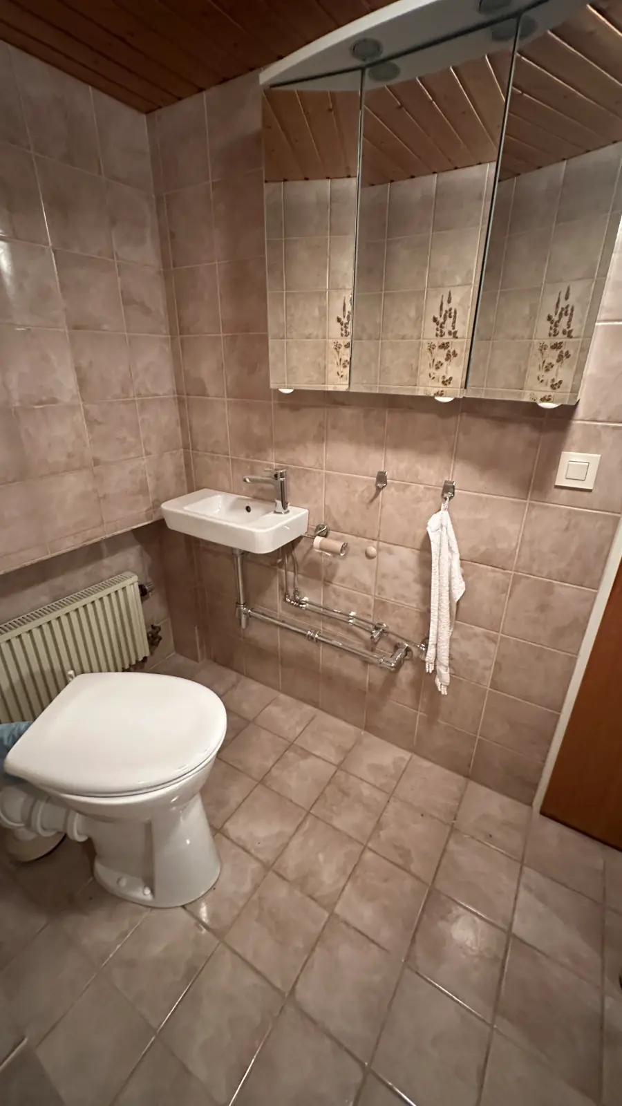 Vorher: Badezimmer im Bestand mit Waschbecken, Spiegelschrank und altem Fliesenspiegel.