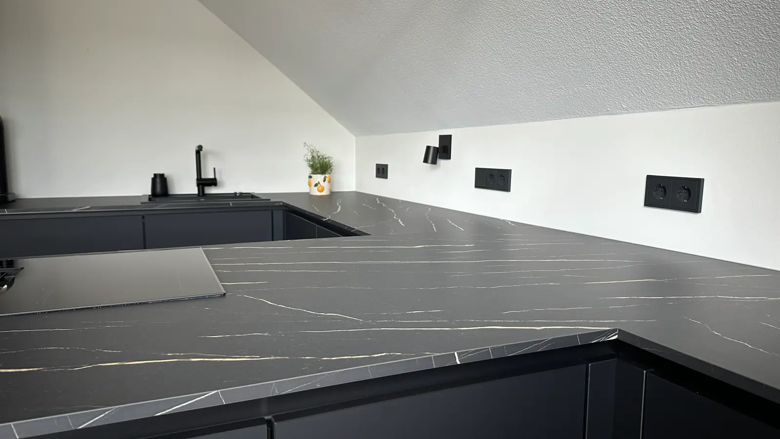 Nachher: Detail der Arbeitsplatte in schwarzer Marmoroptik mit Kochfeld und Spüle.